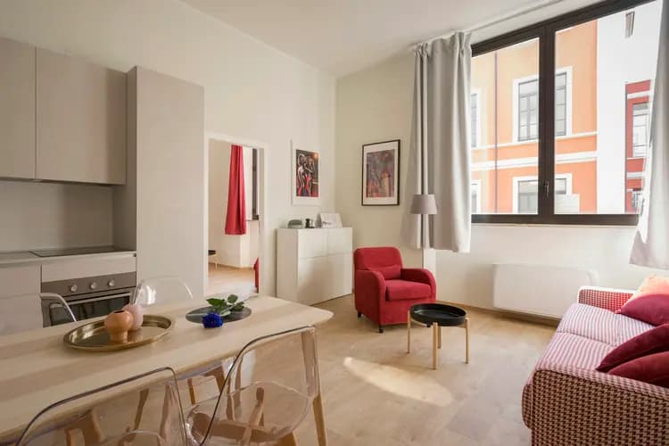 Lichte woonkamer met een rode fauteuil, open keuken en hoge ramen